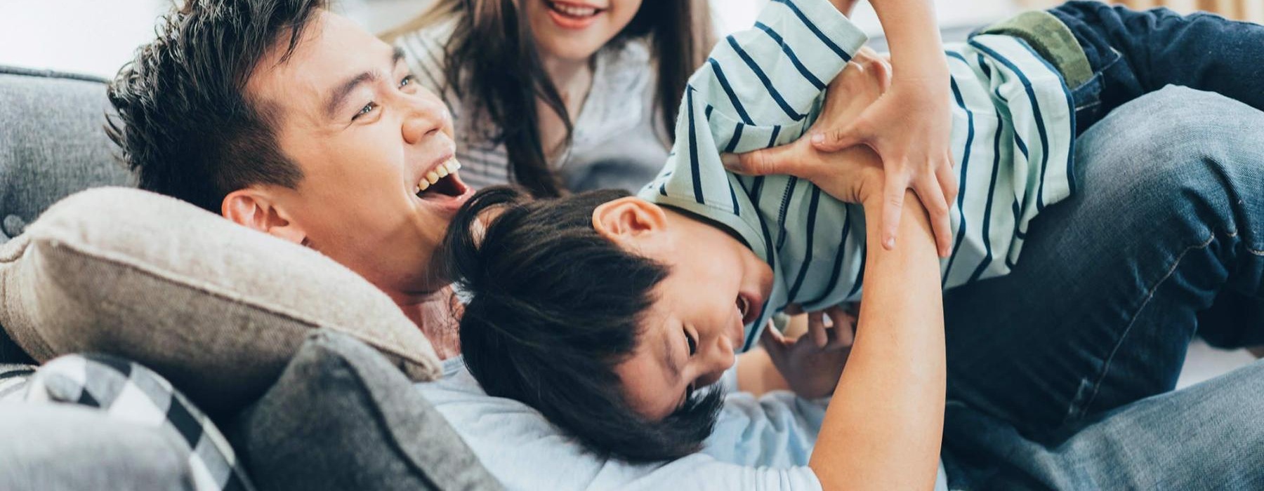 father plays on a couch with his young children